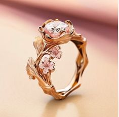 a gold ring with pink flowers and leaves on the side, sitting on top of a table