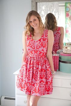 a woman standing in front of a mirror wearing a red dress with white flowers on it