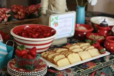 a table topped with plates and bowls filled with cake covered in strawberries on top of it