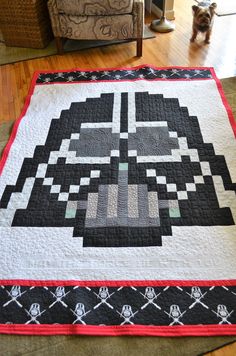 a star wars themed quilt on the floor in a living room with a dog looking at it