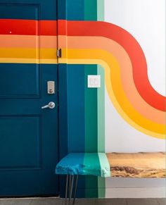 a blue bench sitting in front of a rainbow painted wall with a door and window