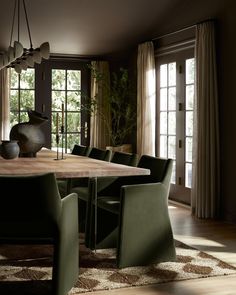 a large wooden table surrounded by green chairs in a room with french doors and windows