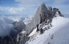 two people climbing up the side of a snow covered mountain with clouds in the background