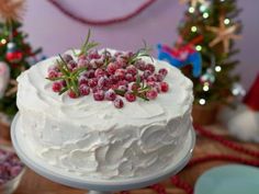 a white frosted cake with berries on top and christmas trees in the back ground