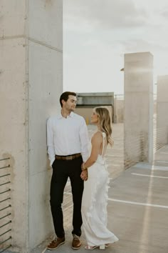 a man and woman standing next to each other in front of a white wall holding hands