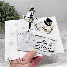 a hand holding up a card with snowman and building blocks on the front, which says let it snow