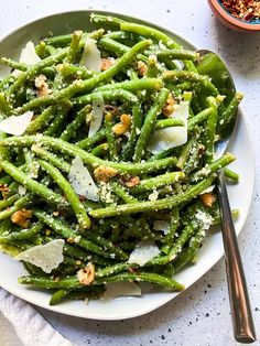 a white plate topped with green beans covered in parmesan cheese and seasoning