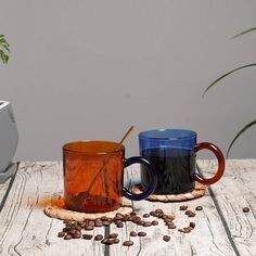 two coffee mugs sitting next to each other on top of a wooden table with beans