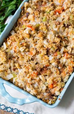 a blue casserole dish filled with stuffing next to parsley and carrots