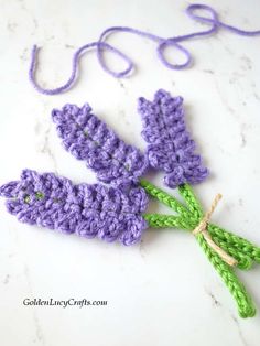 crocheted lavender flowers with green stems on a white countertop next to a purple string