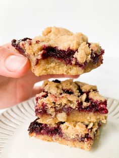 two pieces of blueberry crumb bars on a white plate with a hand holding one