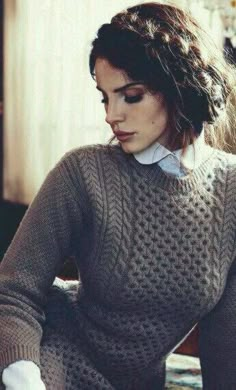 a woman sitting down wearing a sweater and gloves