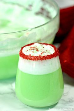 two glasses filled with green liquid and topped with red sprinkles, sitting on a marble surface