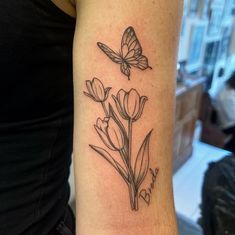 a woman's arm with a butterfly and flowers tattoo on the back of her left arm