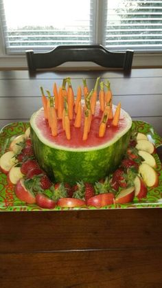 a watermelon with carrots and apples arranged in the shape of a bowl