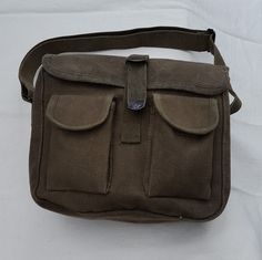 "This simple military style waxed canvas shoulder bag is made from heavy 100% cotton canvas and is treated with a beeswax blend that repels water; treating canvas with wax is a method used since the 1920's to make the material water resistant. It features one large main compartment and two front pockets with hook and loop closures. The main flap closes with a strap and a metal fold over style buckle. The bag measures approximately 10\" across by 8\" tall and 3.5\" wide with a strong 1.5\" wide a Military Canvas Shoulder Bag For Outdoor, Khaki Waxed Canvas Shoulder Bag For Outdoor, Outdoor Khaki Waxed Canvas Shoulder Bag, Khaki Waxed Canvas Bag With Adjustable Strap, Military Style Canvas Shoulder Bag, Military Canvas Shoulder Bag For Everyday Use, Khaki Waxed Canvas Rectangular Bag, Khaki Canvas Shoulder Bag With Waxed Finish, Khaki Waxed Canvas Shoulder Bag With Adjustable Strap