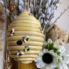 a yellow vase filled with flowers next to a stuffed bear and some branches in the background