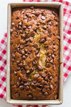 a loaf of chocolate chip banana bread in a pan on a red and white checkered cloth