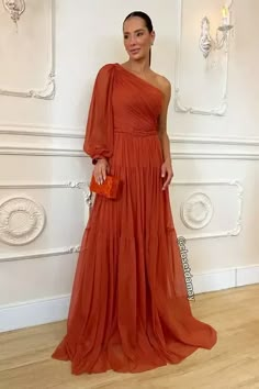 a woman in an orange dress standing next to a white wall and holding a purse