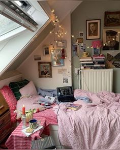 a bed with pink sheets and pillows in a bedroom under a slanted ceiling filled with pictures