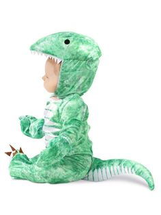 a baby in a green dinosaur costume sitting on the ground with its mouth open and teeth out