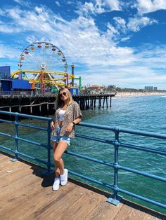 a woman standing on a pier next to the ocean with a ferris wheel in the background