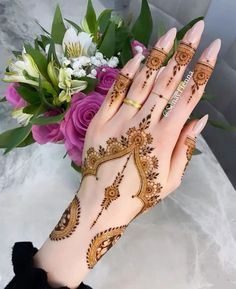 a woman's hand with henna tattoos on it and flowers in the background