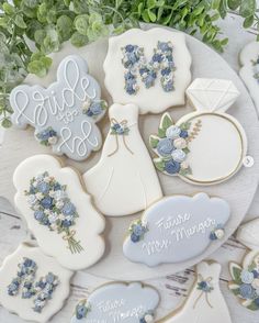 wedding cookies decorated with blue and white frosting on a plate next to greenery