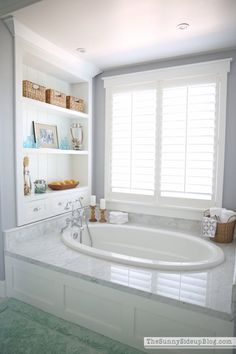 a large white bath tub sitting in a bathroom next to a window with shutters