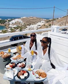 two women sitting on a bench with plates of food and drinks in front of them