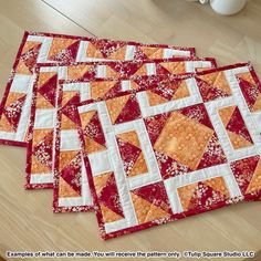 four orange and white quilts are on the floor next to a vase with flowers