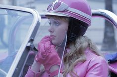 a woman wearing pink gloves and a helmet sitting in a car