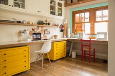 a kitchen with yellow cabinets and white counter tops next to a red chair in front of a window