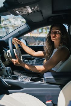 a woman sitting in the driver's seat of a car with her hands on the steering wheel