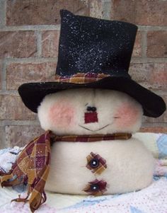 a snowman with a black hat and scarf on it's head, sitting in front of a brick wall