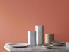 white plates and vases sit on a marble table against an orange painted wall in the background