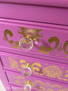 a purple dresser with gold designs and glass knobs on the drawer pulls open to reveal an ornate design