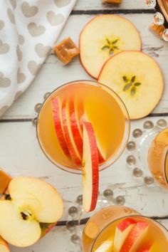 two glasses filled with apple cider next to sliced apples