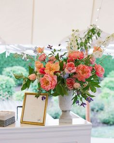 a vase filled with pink and orange flowers on top of a white table under a tent