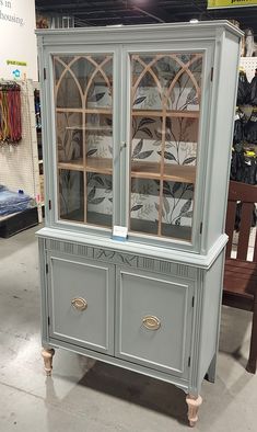 a gray china cabinet with glass doors on display at a furniture store in the middle of a room