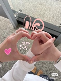 two hands making a heart shape with pink and white hearts on their fingers in front of a mirror