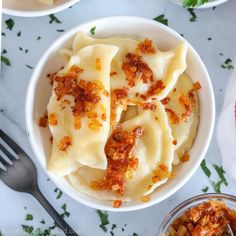 two bowls filled with pasta and sauce on top of a white marble table next to silverware