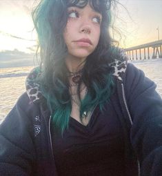 a woman with green hair standing in front of the ocean