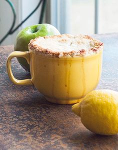 a lemon and an apple sitting on top of a table next to a mug filled with liquid