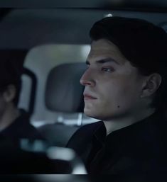 a man sitting in the back seat of a car next to another man wearing a black shirt