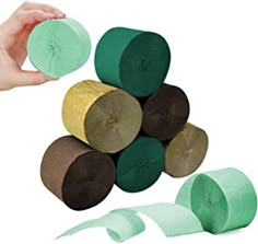 several pieces of green, brown and gold colored toilet paper being held by two hands