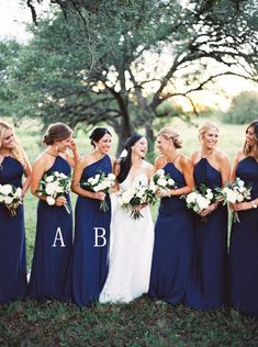 a group of women standing next to each other in front of a tree holding bouquets