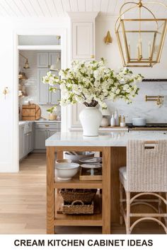 a kitchen with white cabinets and marble counter tops, gold chandelier above the island