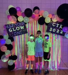 three children standing in front of a backdrop with balloons and streamers on it that says get your glow on