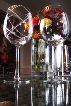 three wine glasses sitting on top of a table next to flowers and vases filled with water